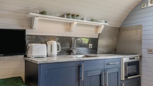 A compact kitchenette with a built-in oven, a sink, and a shelf above the counter holding jars and cups.
