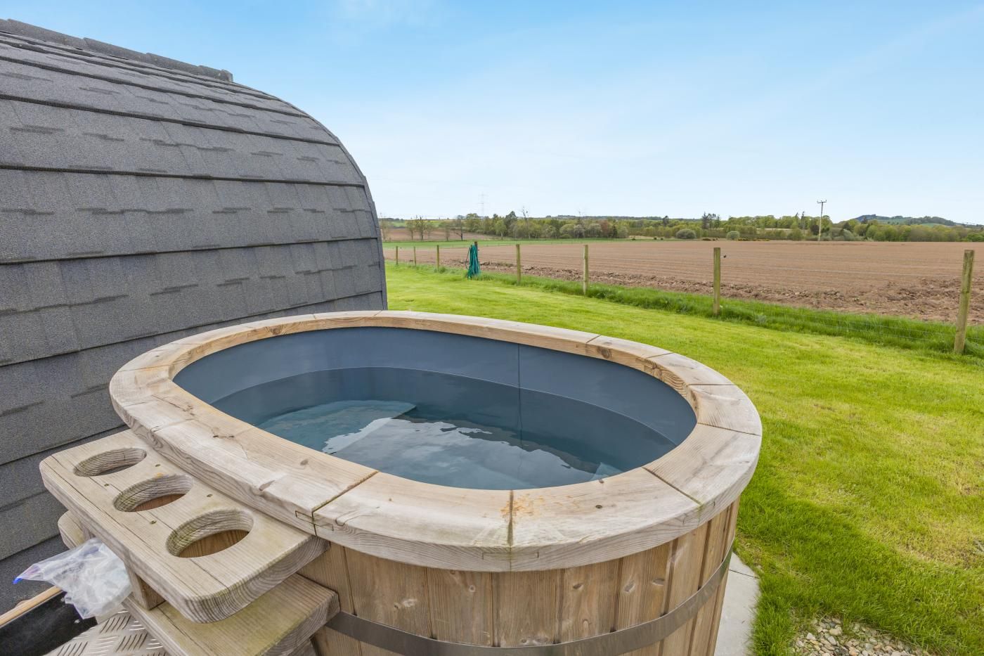 Un bain à remous avec un revêtement extérieur en bois, une zone herbeuse en arrière-plan et un ciel dégagé.