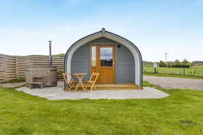A small, single-story structure with a curved roof, a wooden door, and a patio area with a table and chairs.