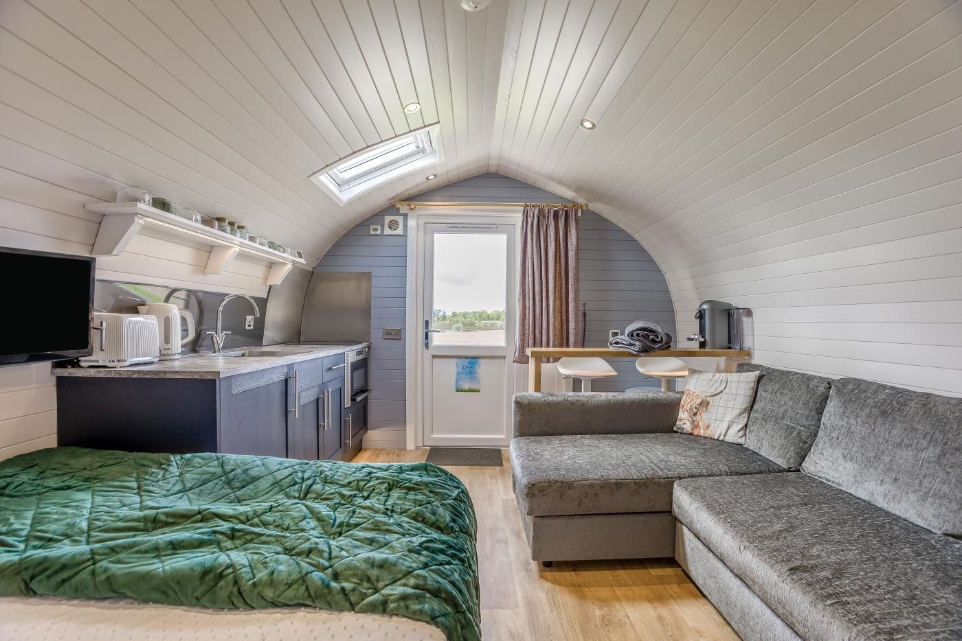A compact, well-lit room with a kitchenette, a sofa, and a bed.