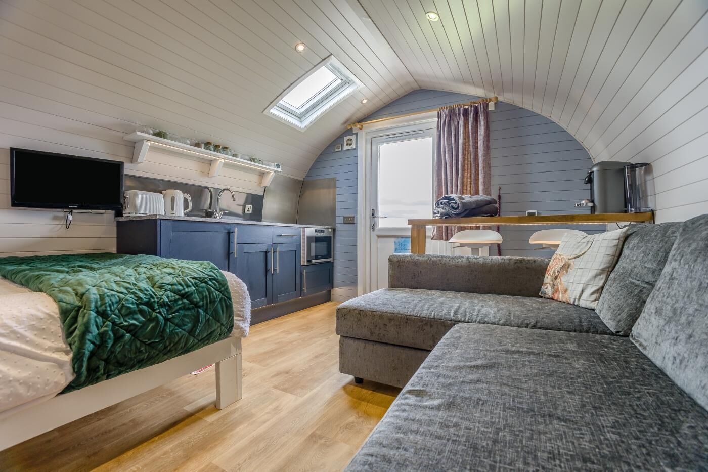 A compact living space with a kitchenette, a bed, a sofa, and a television.