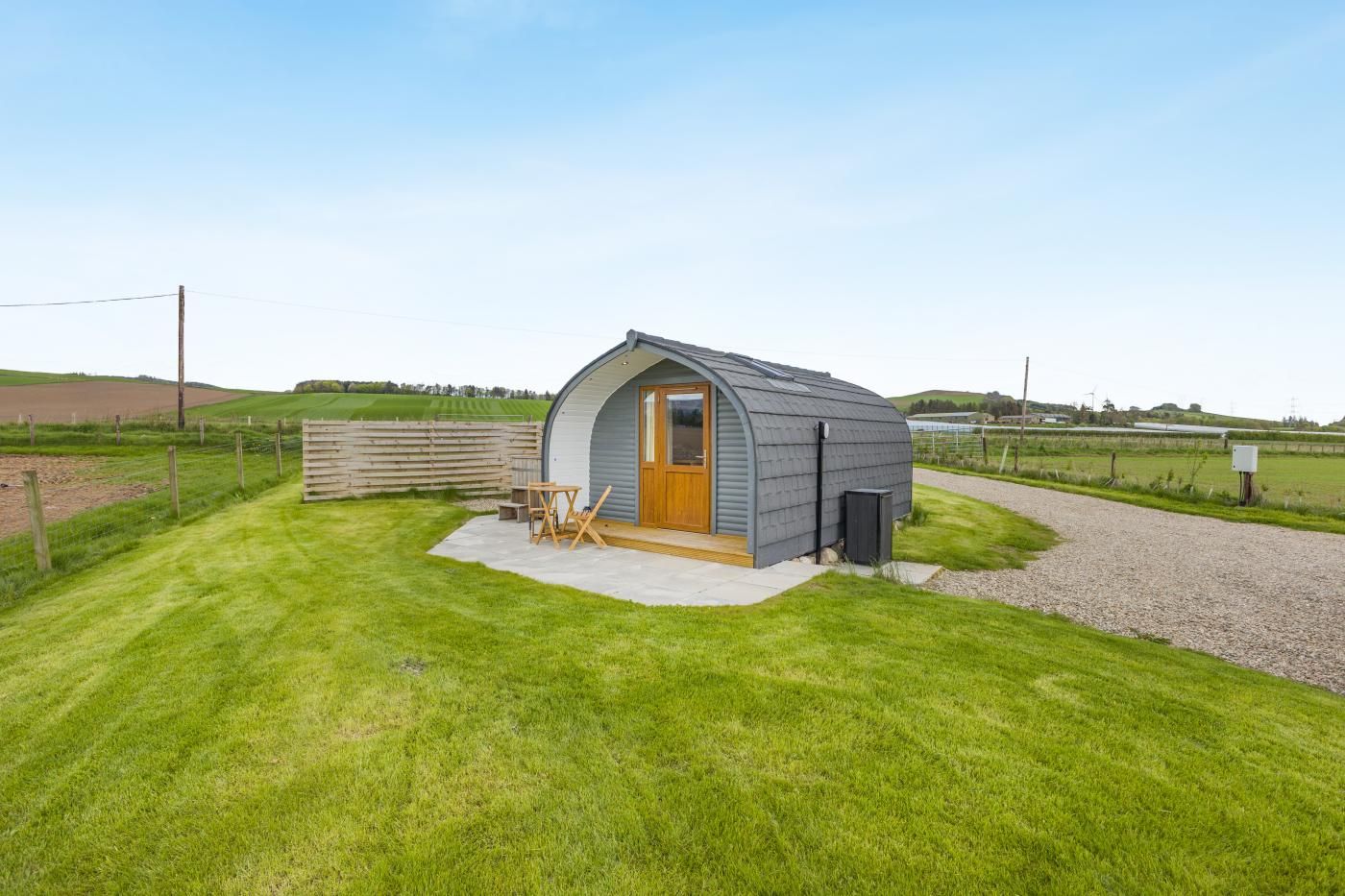 A small, single-story structure with a curved roof, a wooden door, and a concrete patio area with a table and chairs.