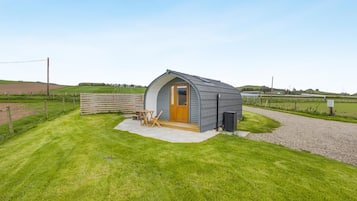 A small, single-story structure with a curved roof, a wooden door, and a concrete patio area with a table and chairs.