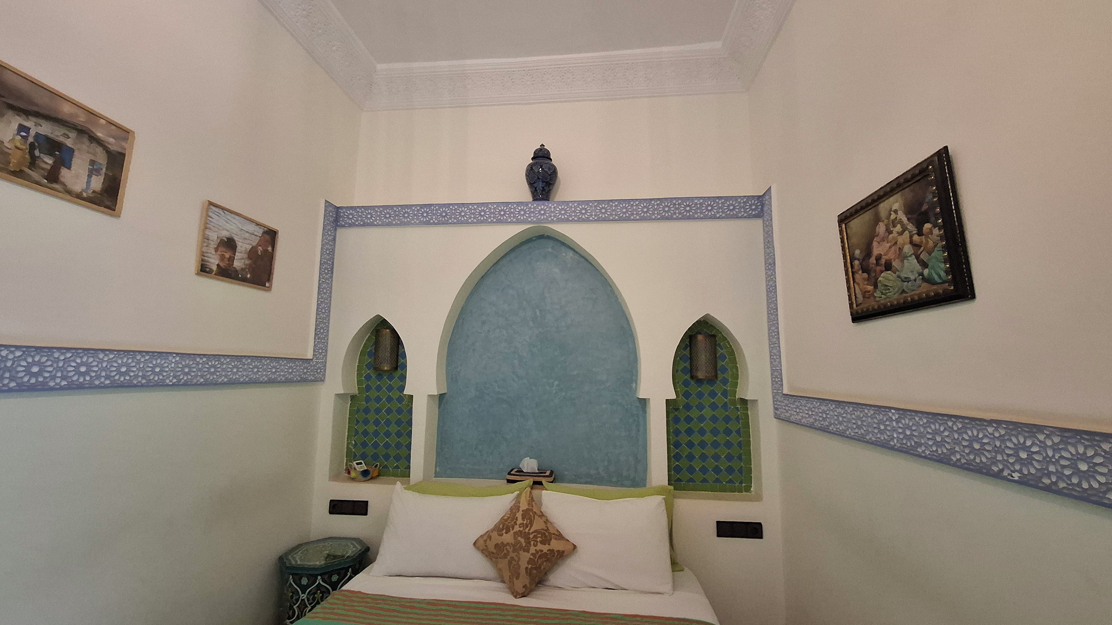 Una habitación con una cama, una mesita de noche, un jarrón decorativo y dos marcos de cuadros en la pared.