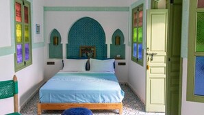 Un dormitorio con cama, una puerta y un ventanal con vidrios de colores.