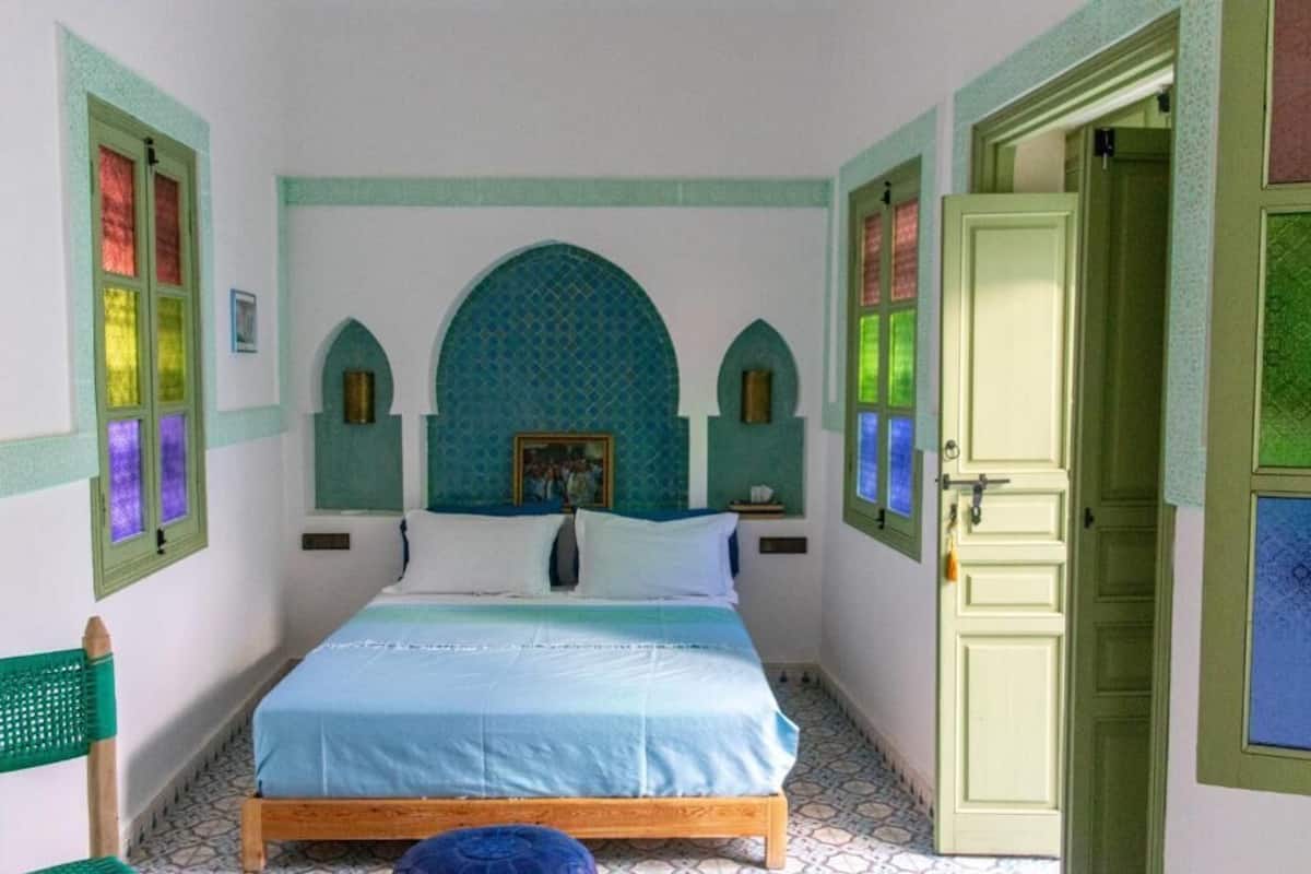 A bedroom with a bed, a door, and a window with colored glass panes.
