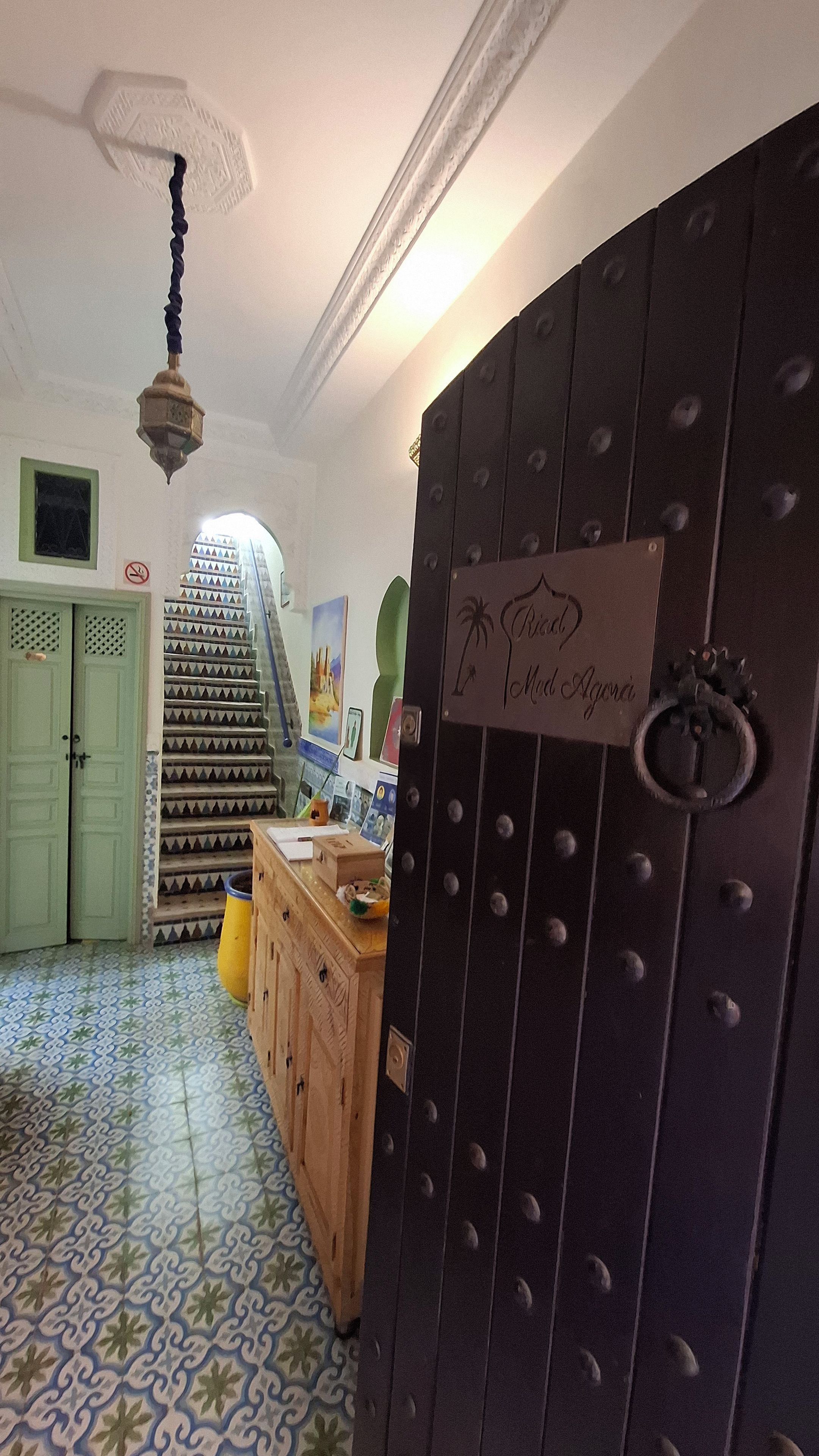 Una scala con un pavimento decorato che conduce a un pianerottolo, un armadietto in legno e una porta con un cartello.