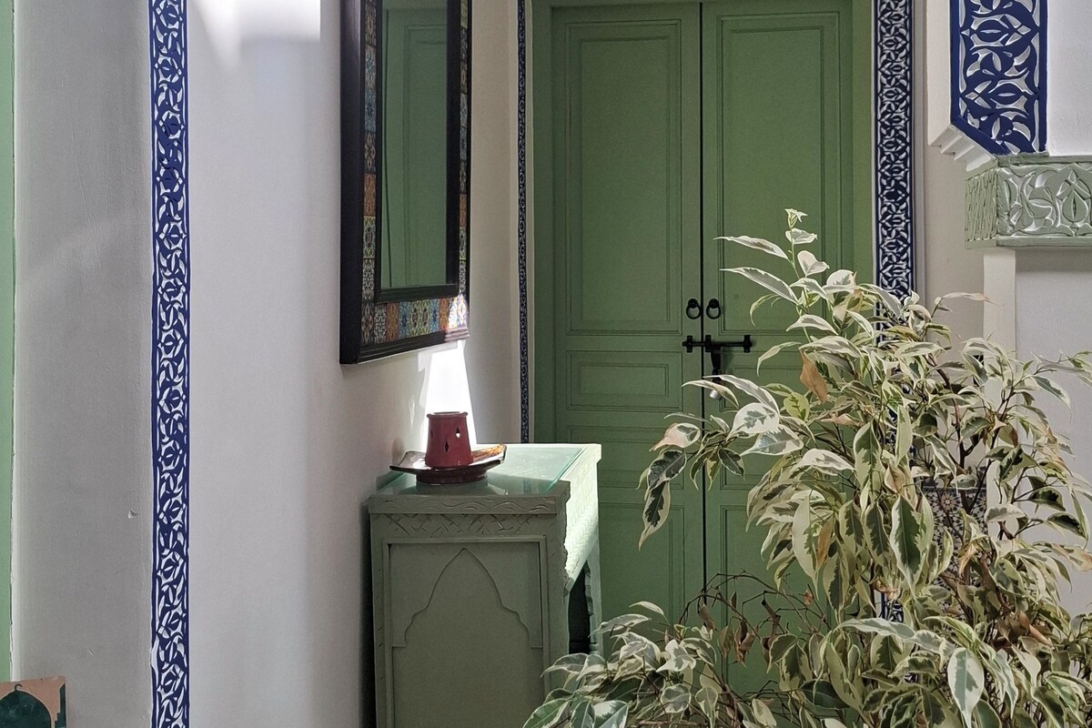 Un pasillo con paredes con diseño, una puerta verde, un espejo y una planta en maceta.