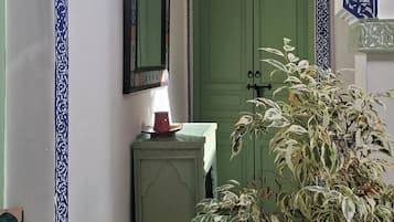 Un pasillo con paredes con diseño, una puerta verde, un espejo y una planta en maceta.