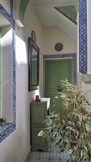 Un pasillo con paredes con diseño, una puerta verde, un espejo y una planta en maceta.