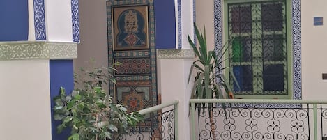 A multi-level interior with ornate blue and white tile work, a balcony with a potted plant, and a door with intricate designs.