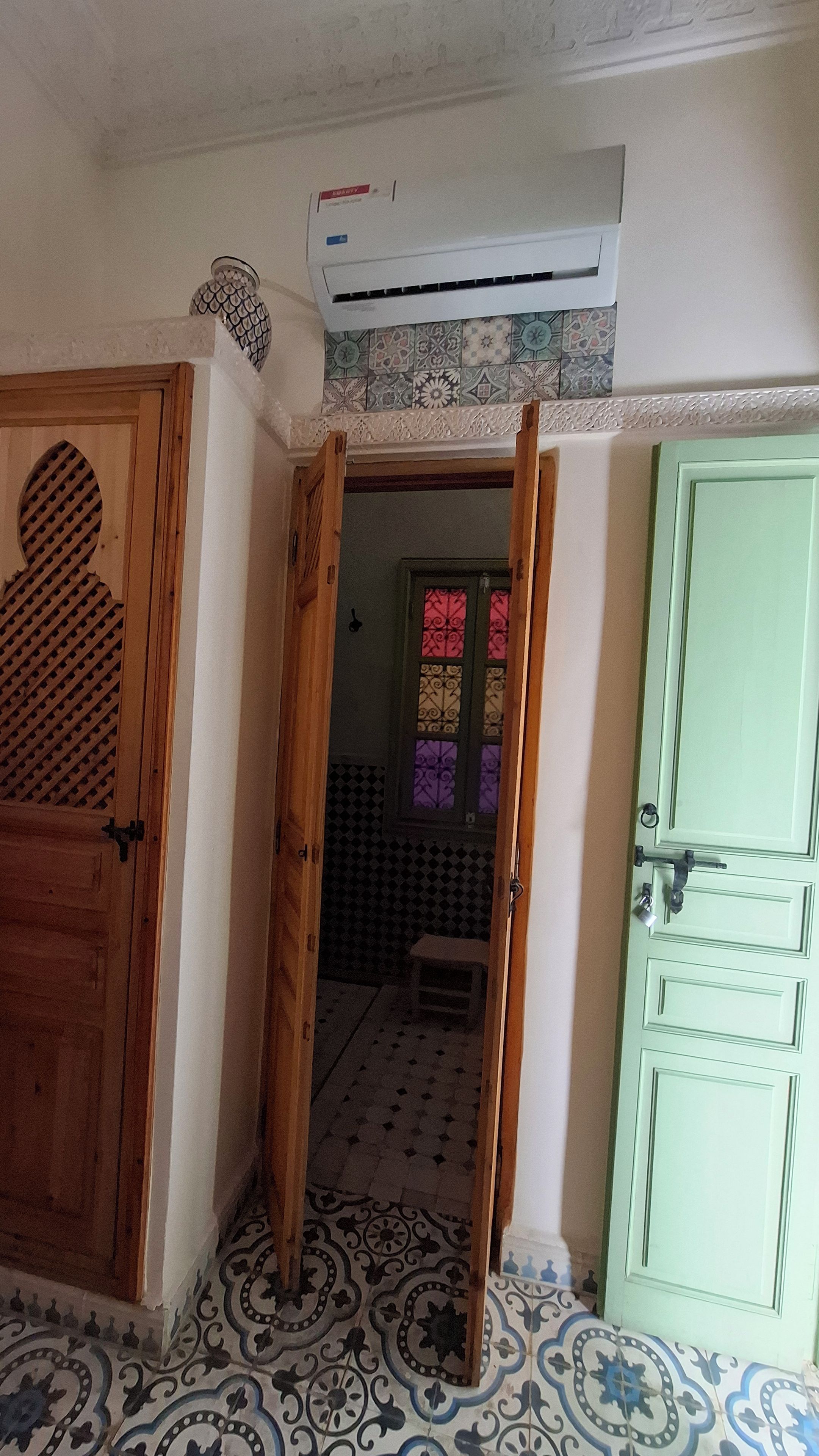 Una stanza con un pavimento decorato, una porta verde e un condizionatore d'aria sopra un muro piastrellato.