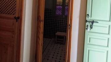 Una stanza con un pavimento decorato, una porta verde e un condizionatore d'aria sopra un muro piastrellato.