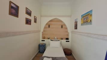 Una camera d'albergo stretta con una testiera in legno, un letto, un piccolo comodino, un cuscino decorativo e una mensola a parete.