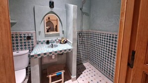 Un baño con piso de baldosas, un lavamanos con espejo, inodoro y ducha.