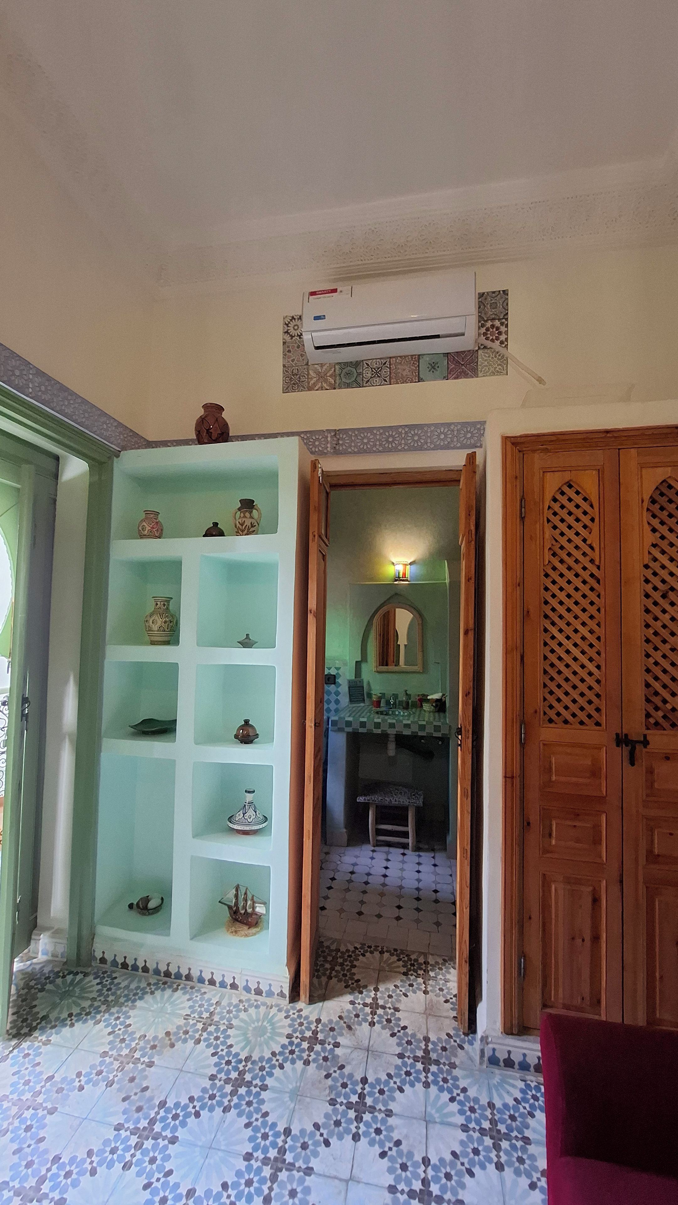 Un pasillo con piso de baldosas, una puerta de madera y una repisa con objetos decorativos.