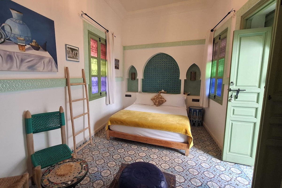 Un dormitorio con cama, una escalera, una silla, una mesita y una puerta.