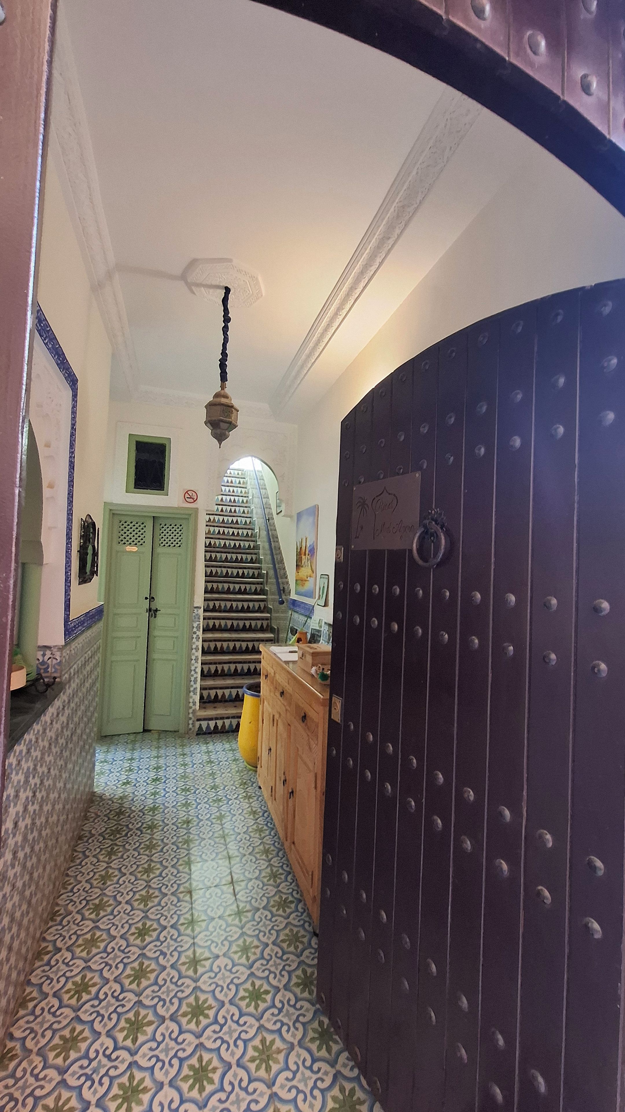 Un corridoio con una porta verde, una scala e una porta scura con un cartello.