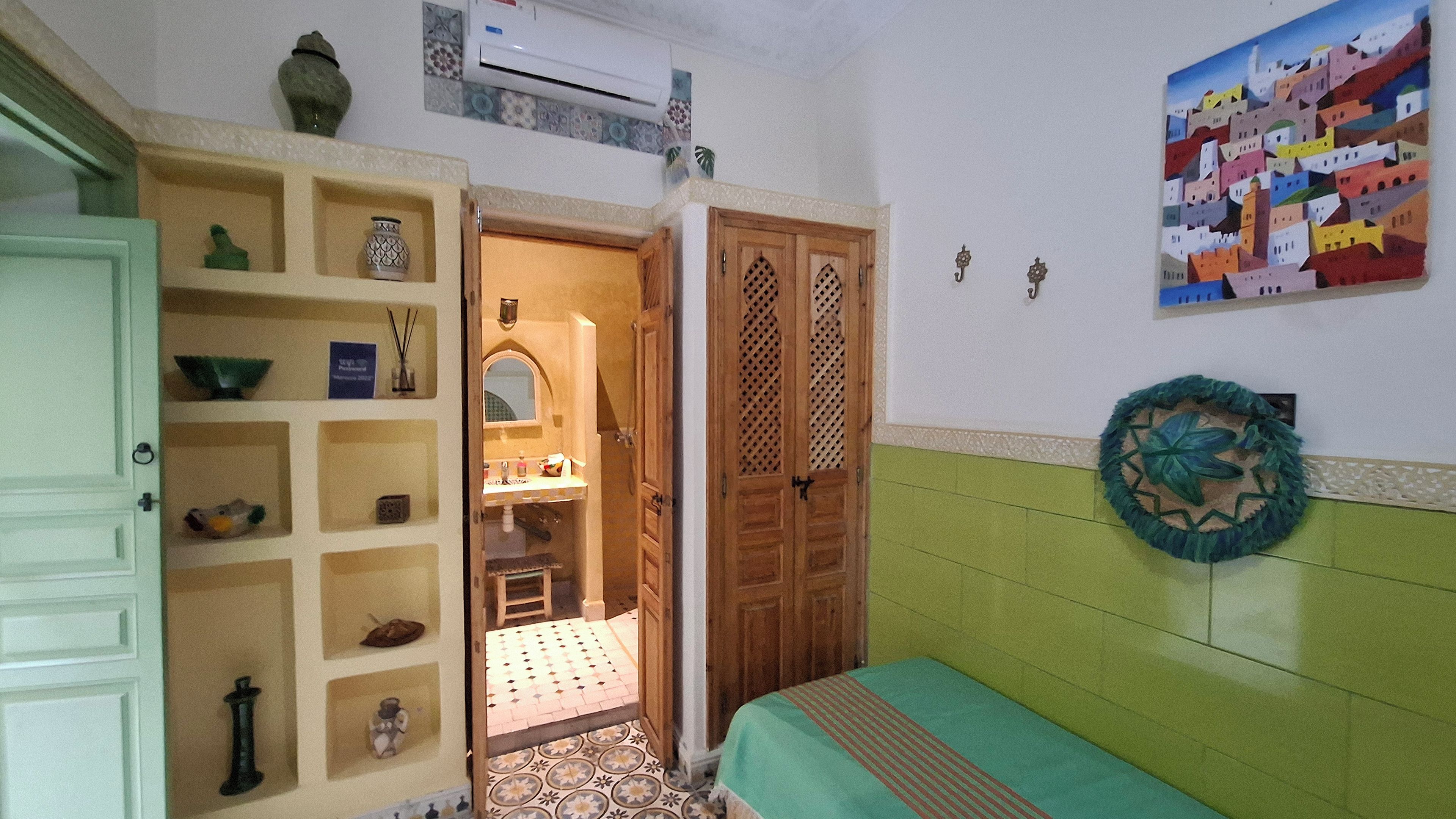 Quarto com uma cama, um armário com diversos objetos, uma porta para um banheiro e uma parede com um prato decorativo.