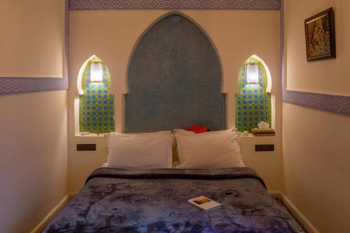 A room with a bed, two nightstands, a window with a decorative frame, and a wall-mounted picture.