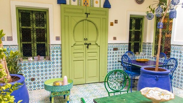 Un patio marroquí tradicional con una puerta verde, paredes con azulejos y mobiliario azul y verde.