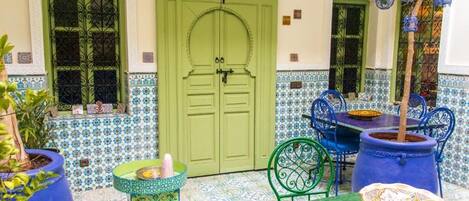 A traditional Moroccan courtyard with a green door, tiled walls, and blue and green furniture.