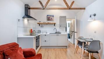 A compact kitchen with white cabinetry, a black range hood, and a dining area with a table and chairs.