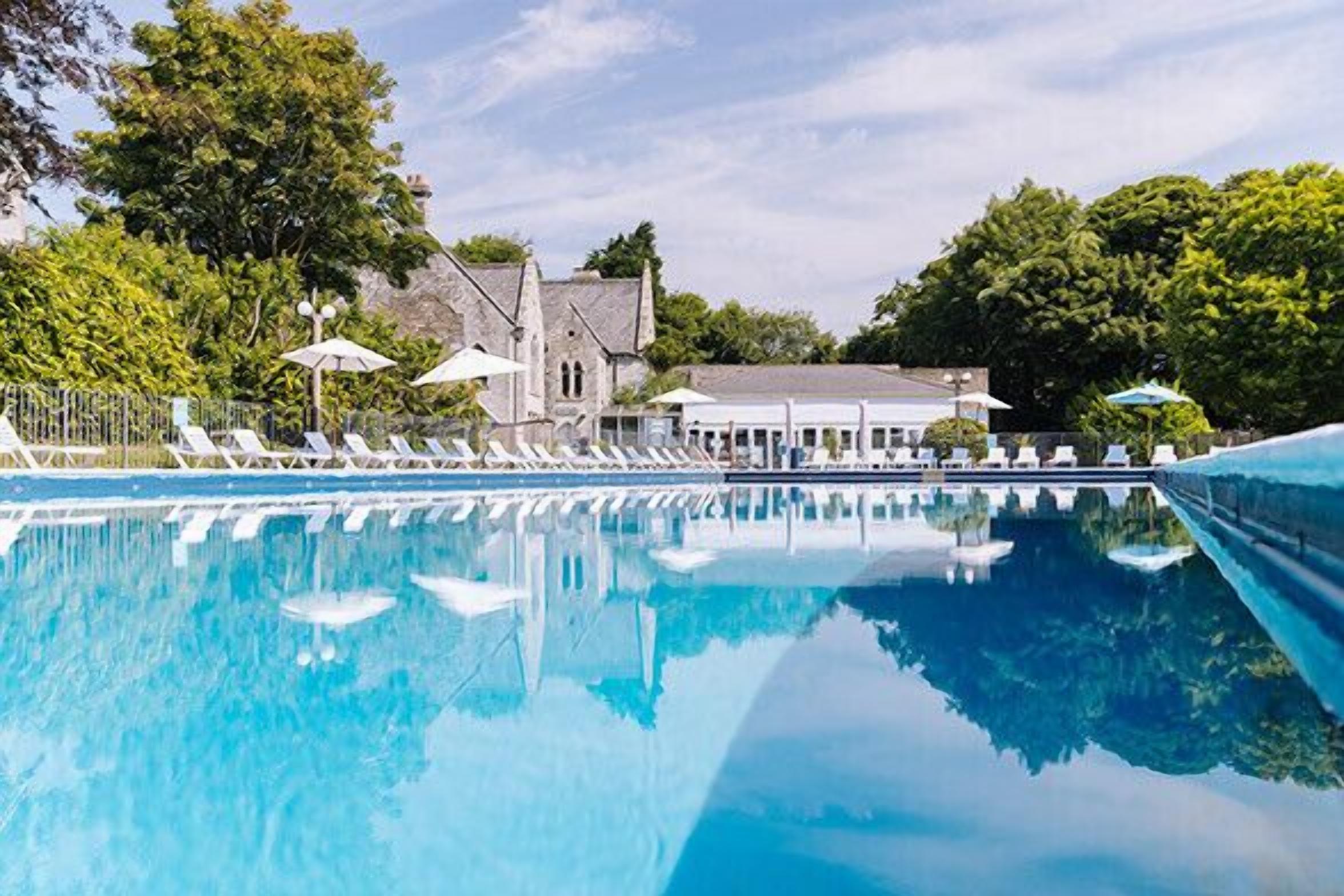 Ein Swimmingpool mit Liegestühlen und Sonnenschirmen, umgeben von Bäumen und einem Gebäude mit Dach.