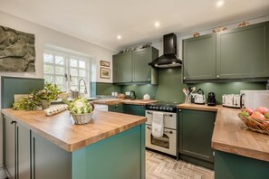 A kitchen with green cabinets, a central island, a stove, and various kitchen appliances. - 2 Bed in Sizewell (oc-w34607) (Sizewell)