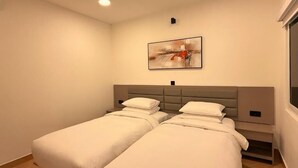 A room with two beds, a headboard, a painting, and a window.