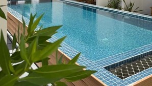 A swimming pool with a tiled edge, surrounded by a building with a door and windows, and a view of trees in the background.