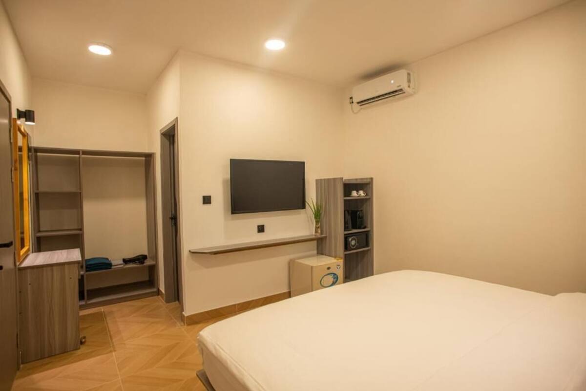 Un dormitorio con cama, televisor montado en la pared, armario y un mueble auxiliar.