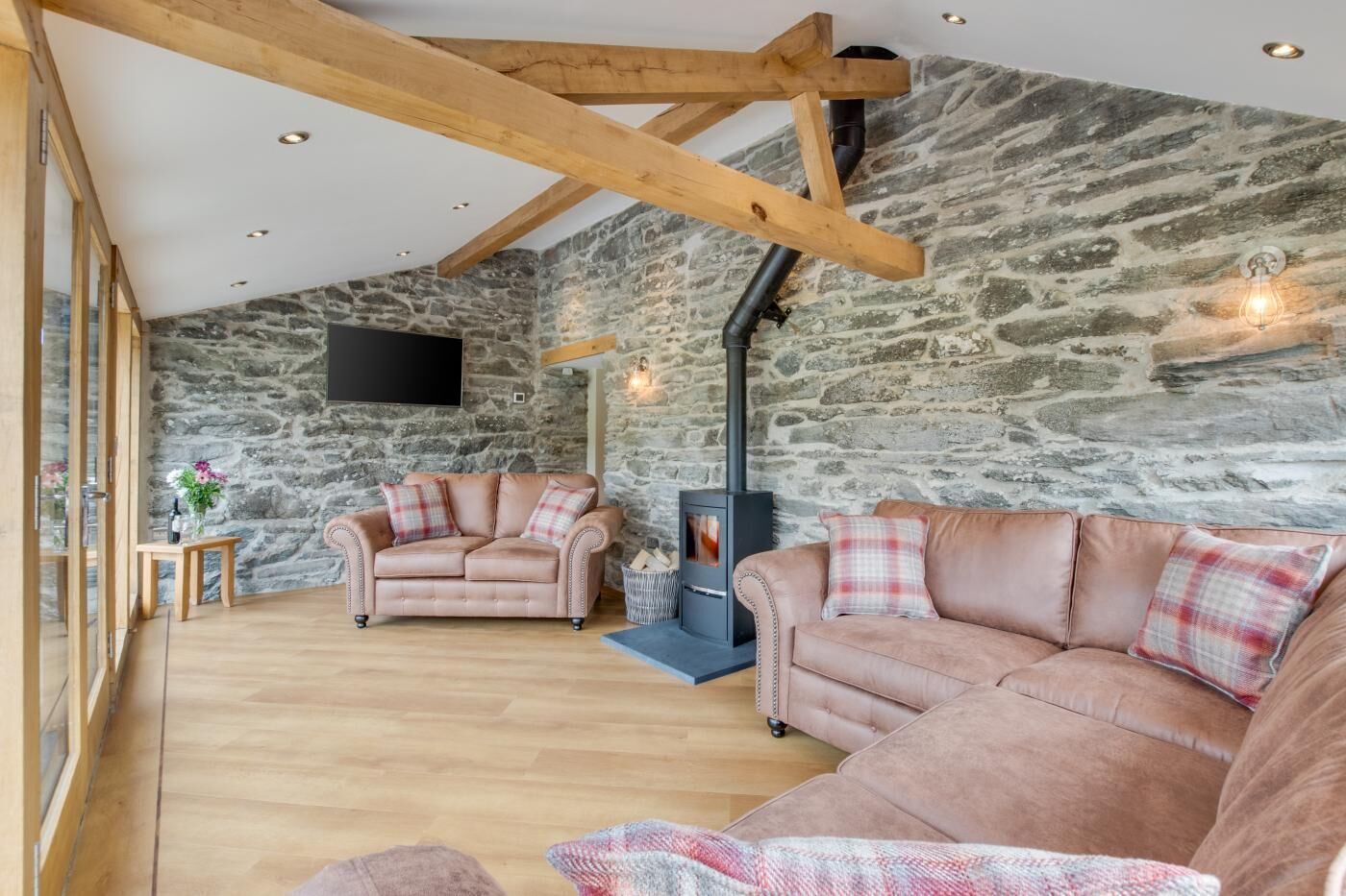 A cozy living room with stone walls, wooden beams, a fireplace, and two leather sofas.