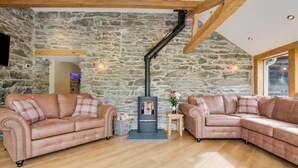 A cozy living room with stone walls, two leather sofas, a small table, and a fireplace. - 3 Bed in Bala (oc-bow69) (Bala)