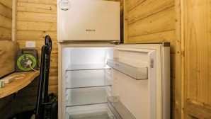 Ein kleines Zimmer mit einem weißen Kühlschrank, einem Staubsauger und einem kleinen Heizgerät an einer Holzwand.