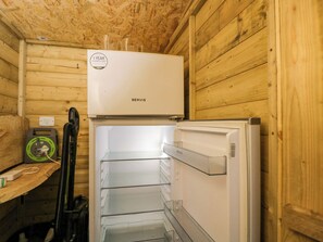 Ein kleines Zimmer mit einem weißen Kühlschrank, einem Staubsauger und einem kleinen Heizgerät an einer Holzwand.