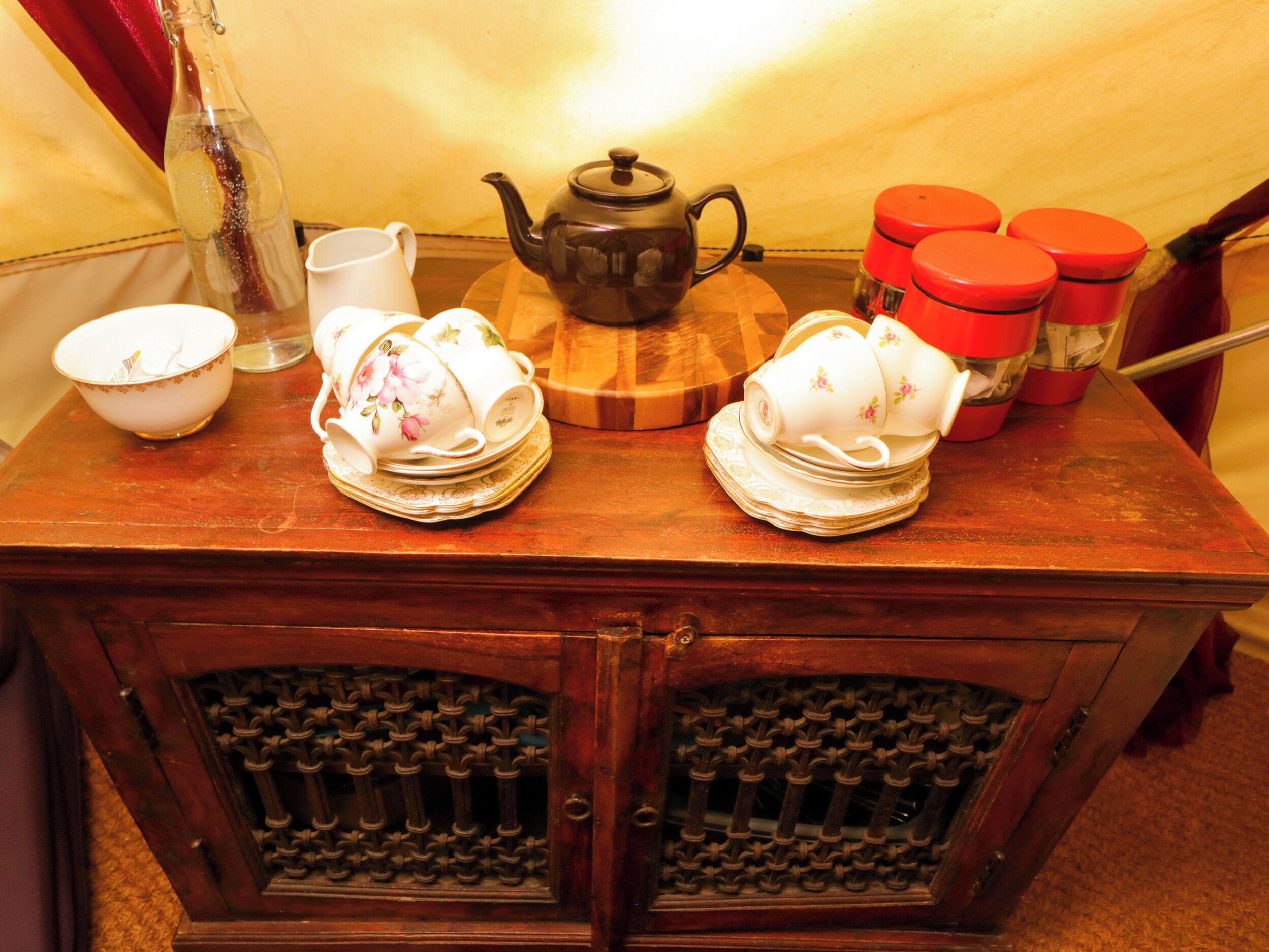 A wooden table with a teapot, cups, and a bottle.
