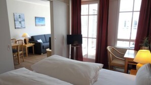 Quarto de hotel com duas camas, um sofá, uma televisão e um espaço de jantar com cadeiras e uma mesa.