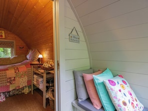 Ein gemütliches Zimmer mit Holzbalkendecke, einem Bett mit floralem Überwurf, einem Nachttisch mit Lampe und einem Schild, das Gäste willkommen heißt.