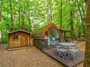 A wooden cabin with a small porch and a table with chairs. - Bluebell Glamping Pod (Newbury)