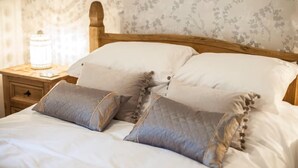 A neatly made bed with a wooden headboard, a bedside table with a lamp, and floral wallpaper. - 3 Bed in Stoney Middleton (oc-c34611) (Stoney Middleton)