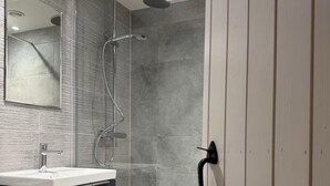 Ett modernt badrum med en dusch som är avskärmad med glasväggar, ett vitt handfat och en spegel.