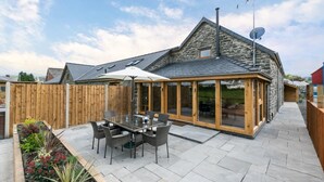 Una casa de piedra con un patio, una zona de comedor con sillas y una mesa, y una cerca de madera.
