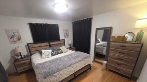 Een slaapkamer met een houten bed, een nachtkastje met een lamp, een dressoir en een spiegel.