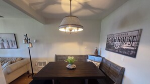 Een eetgedeelte met een donker houten tafel, bankzitplaatsen, een hangende lamp en een bord aan de muur.