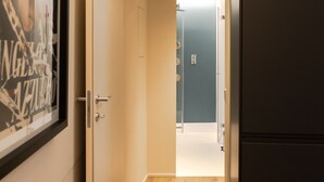 A hallway with a wooden floor, a framed picture on the left, a black refrigerator on the right, and a door at the end leading to a bathroom. - Apartment 'Flat 1' with Wi-Fi and Air Conditioning (Portese)