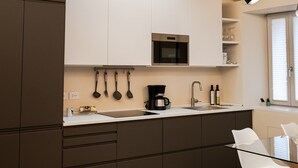 A modern kitchen with wooden beams, a skylight, white cabinets, a black microwave, and a glass table with chairs. - Apartment 'Flat 1' with Wi-Fi and Air Conditioning (Portese)