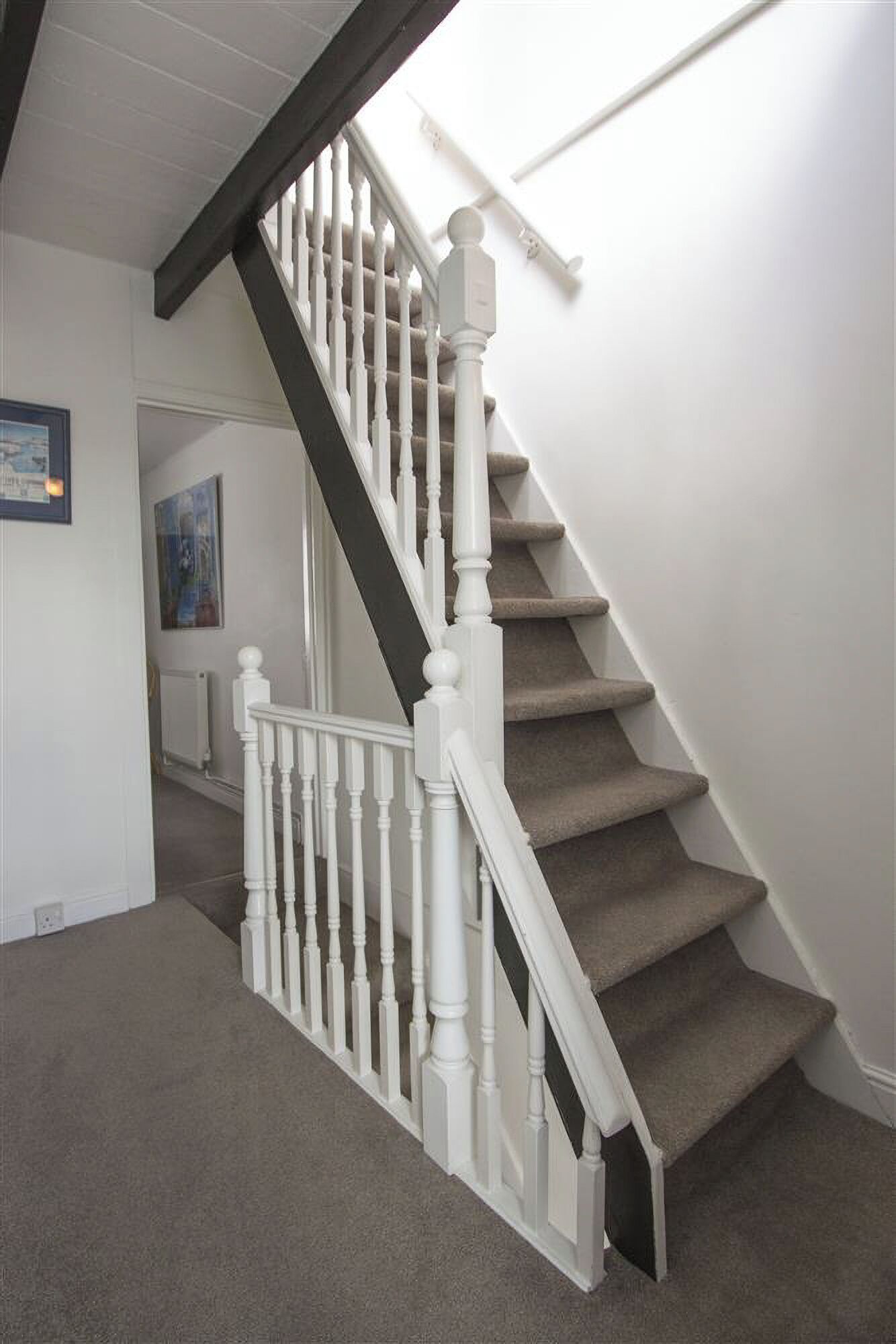Een trap met witte balustrades en een donkere leuning, bekleed met tapijt, met een witte muur en een ingelijst beeld.
