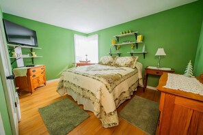 Ein Schlafzimmer mit einem Bett, einem Holzschrank, Nachttischen, einem Fernseher und grünen Wänden.