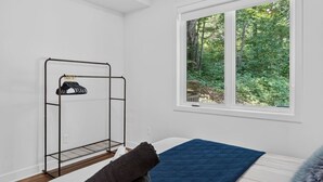 Een kamer met een bed, een raam met uitzicht op een bos en een metalen rek.